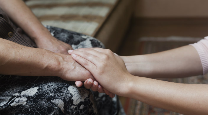 Two sets of hands/arms clasped across a lap in a gesture of support